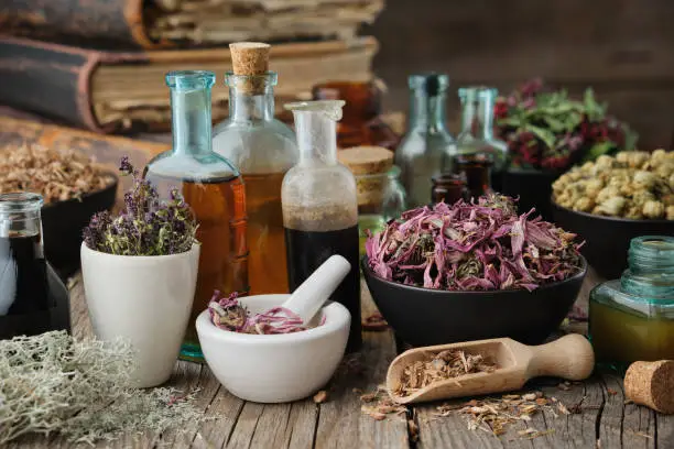 Bottles of healthy tincture or infusion, mortar and bowls of medicinal herbs, old books on wooden table. Herbal medicine.