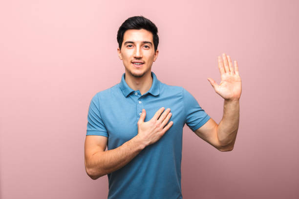 joven guapo con sonrisa neutral con la mano en el pecho dando juramento - made man object fotografías e imágenes de stock