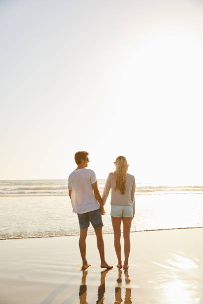 istock Couple holding hands while walking along a beach in the afternoon 1211592250
