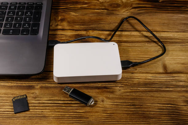 istock External HDD connected to laptop computer, SD memory card and USB flash drive on a wooden desk. Concept of data storage 1211592317