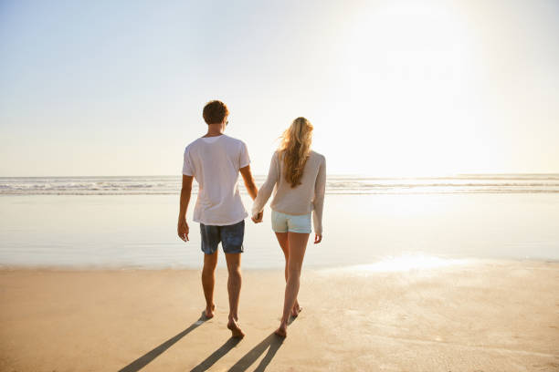 istock Young couple holding hands and walking on a sandy beach 1211594274