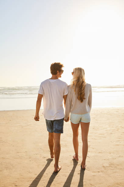 istock Young couple walking hand in hand together on a beach 1211594423