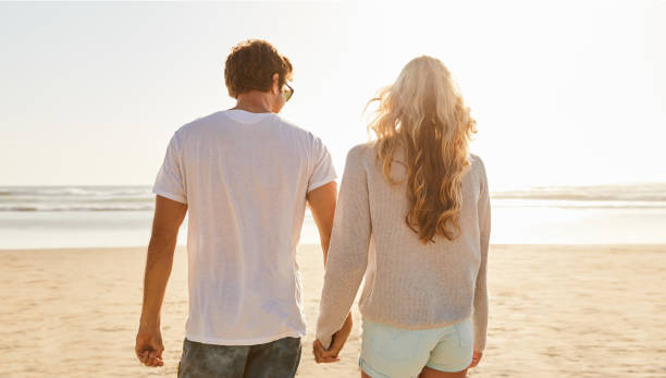 istock Young couple walking hand in hand together on a sandy beach 1211594598