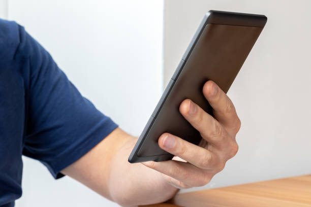 istock Gray e-reader electronic book in male hand. A man in a blue t-shirt with a tablet. Selective focus 1211595407