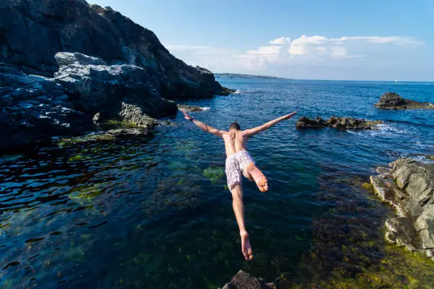 Photo of Two young men jumping off cliff into sea