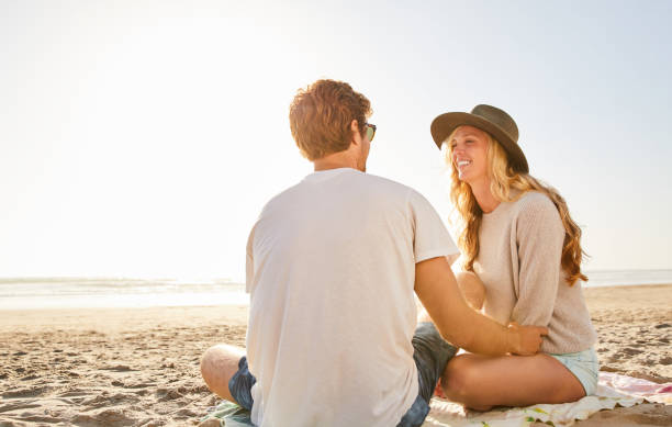 istock Smiling young couple sitting together at the beach 1211596040