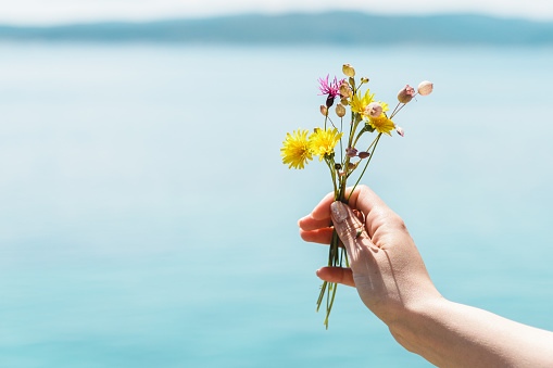 closeup woman hand holding a bouquet of spring wildflowers with ocean in background