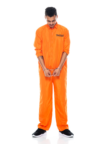 Full length of aged 20-29 years old african-american ethnicity young male criminal standing in front of white background wearing uniform who is sulking and using handcuffs