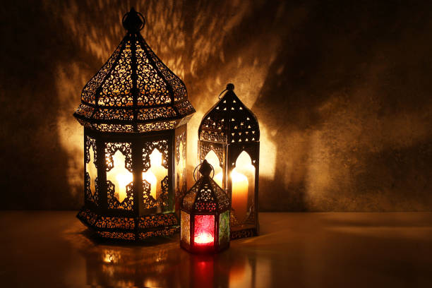 istock Ornamental Arabic lanterns with burning candles on table glowing at night. Festive greeting card, invitation for Muslim holy month Ramadan Kareem. Iftar dinner background with golden glow. 1211597939