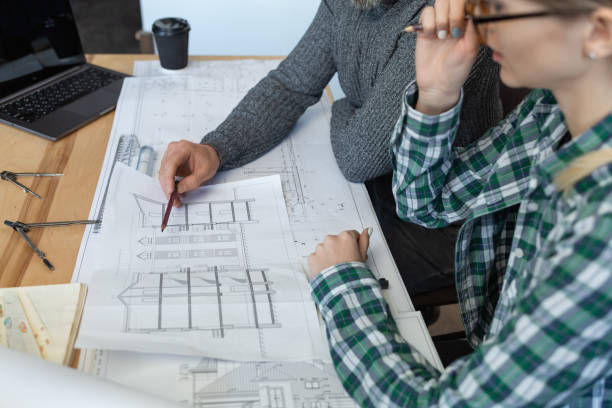 istock Interior designers team working in office with blueprints and architect equipment, sketching, negotiating and planning construction project. Partners discussing at work. Business construction concept 1211598022