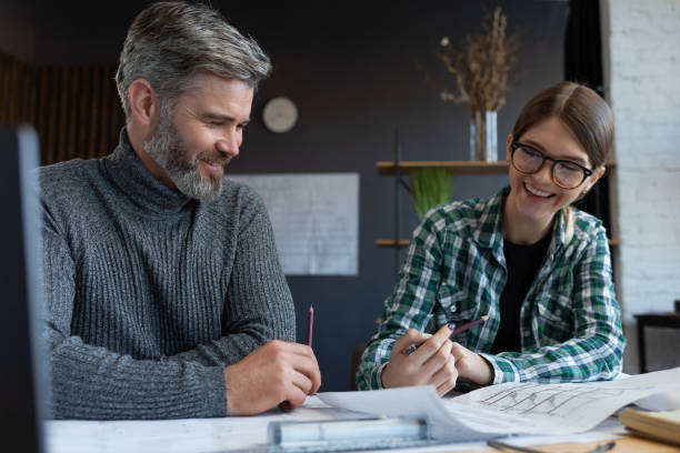 istock Interior designers team working in office with blueprints and architect equipment, sketching, negotiating and planning construction project. Partners discussing at work. Business construction concept 1211598036