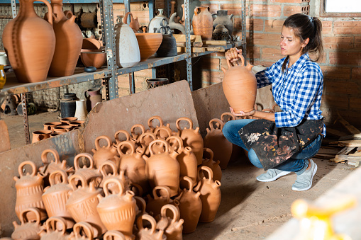 Portrait of female potter holding and inspecting ceramics in pottery workshop