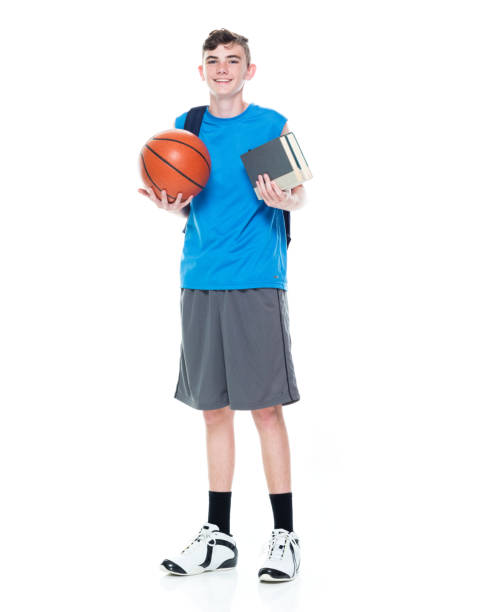 istock Caucasian young male university student walking in front of white background wearing backpack and holding textbook and using sports ball 1211601196
