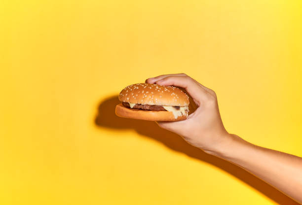 istock Hand holding burger isolated on light yellow background .studio shot. 1211601643