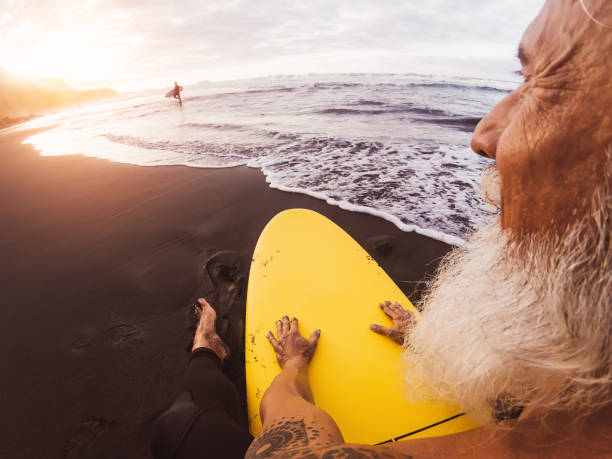 istock Happy surfer senior sitting on surfboard watching sunset time - Mature bearded man having fun on surfing day - Extreme sport and health people lifestyle concept 1211602885