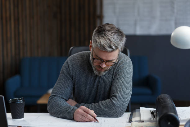 istock Interior designer working in office with blueprints.Engineer inspect architectural plan, sketching a construction project.Portrait of handsome bearded man at workplace. Business construction concept 1211603001