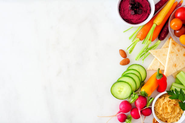 istock Selection of fresh vegetables and hummus, top view side border on a white marble background 1211604262