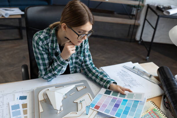 istock Female interior designer working in office with color palette. Architect select colors for building using color swatches, searching new ideas for project. Portrait of beautiful woman at workplace 1211604733