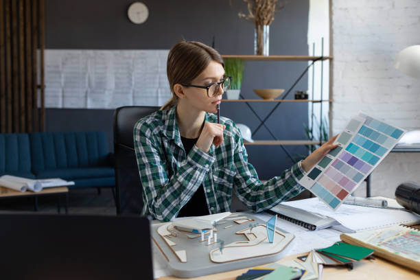 istock Female interior designer working in office with color palette. Architect select colors for building using color swatches, searching new ideas for project. Portrait of beautiful woman at workplace 1211604865