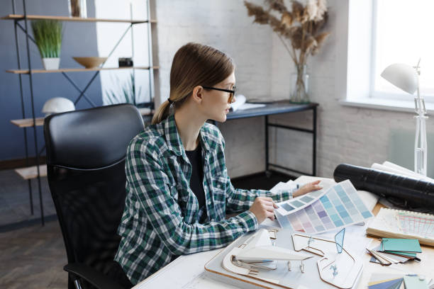 istock Female interior designer working in office with color palette. Architect select colors for building using color swatches, searching new ideas for project. Portrait of beautiful woman at workplace 1211604933