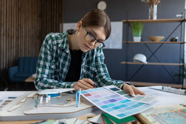 istock Female interior designer working in office with color palette. Architect select colors for building using color swatches, searching new ideas for project. Portrait of beautiful woman at workplace 1211604971