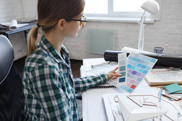 istock Female interior designer working in office with color palette. Architect select colors for building using color swatches, searching new ideas for project. Portrait of beautiful woman at workplace 1211604985