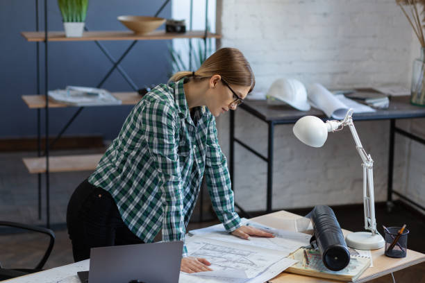 istock Interior designer working in office with blueprints.Engineer inspect architectural plan, sketching a construction project.Portrait of beautiful woman at workplace. Business construction concept 1211605220