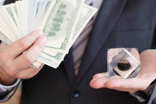 Businessman in suit, tie holds in hands drop of black oil of Brent brand in crystal cube.Pack of hundred dollars bills.Crisis in financial market,falling,rising prices,quotes,changes in exchange rate. hombre de negocios en traje, corbata sostiene en las manos gota de aceite negro de la marca brent en cubo de cristal. un paquete de billetes de cien dólares. crisis en el mercado financiero, caída, aumento de precios, cotizaciones, cambios en el tipo de