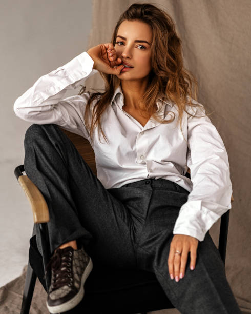 Fashion model sitting chair in classic trausers and white shirt. Stylish woman beauty portrait in studio on white background Fashion model sitting chair in classic trausers and white shirt. Stylish woman beauty portrait in studio on white background Women's Dress Shirt stock pictures, royalty-free photos & images