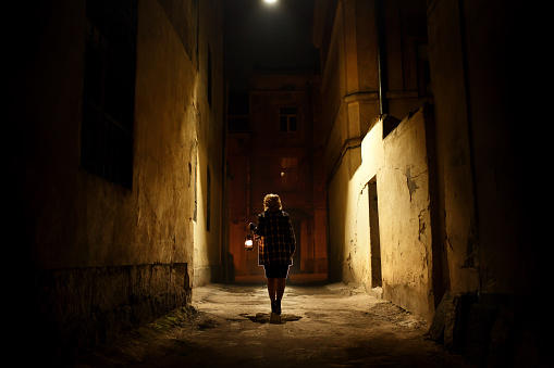 Mysterious blonde woman in elegant retro coat with old oil lantern walking in old French street in Paris, noire atmosphere, investigating crime, detective concept