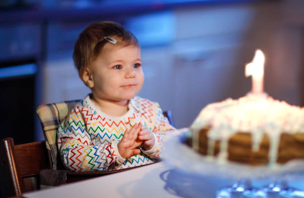 첫 번째 생일을 축하하는 귀여운 아름다운 어린 소녀. 집에서 만든 구운 케이크에 촛불 하나를 불고 아이, 실내. 사랑스러운 유아 아이, 아름다운 딸을위한 생일 가족 파티 - first birthday 뉴스 사진 이미지