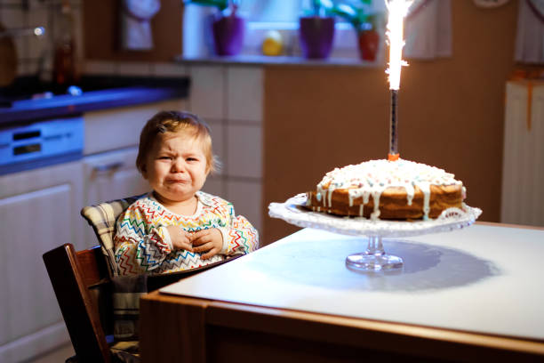 uma garotinha chorando linda comemorando o primeiro aniversário. criança assustada e com medo de fogos de artifício em bolo assado, dentro de casa. criança chil não feliz - birthday cake family germany indoors - fotografias e filmes do acervo