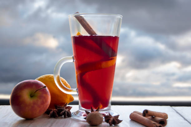 A glass of mulled wine with apple, lemon, cinnamon and star anise, against a gray sky. A glass of mulled wine with apple, lemon, cinnamon and star anise. Gray sky background. кружка stock pictures, royalty-free photos & images