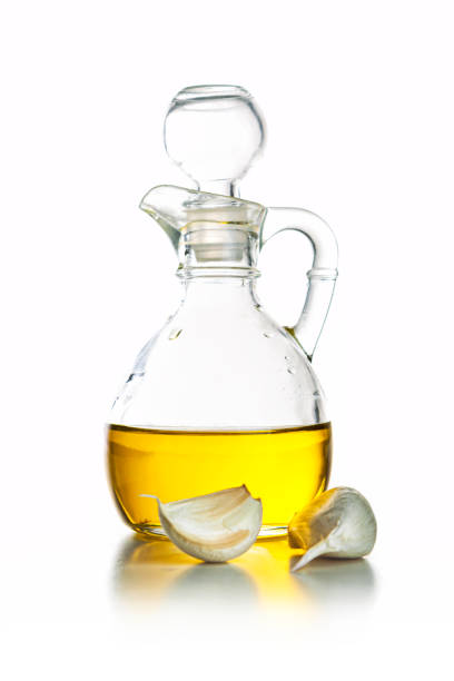Cooking and seasoning: high angle view of extra virgin olive oil in a glass gravy boat with a rosemary twig, garlic cloves, parsley and mixed peppercorns around it isolated on reflective white background. Olive tree branches and three green olives complete the composition. The composition is at the right of an horizontal frame leaving useful copy space for text and/or logo at the left. Predominant colors are yellow, green and white. High resolution 42Mp studio digital capture taken with Sony A7rII and Sony FE 90mm f2.8 macro G OSS lens