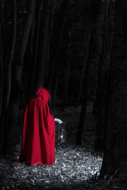 Attractive woman dressed a little red riding-hood walk in a dark forest with a lantern - fotografia de stock