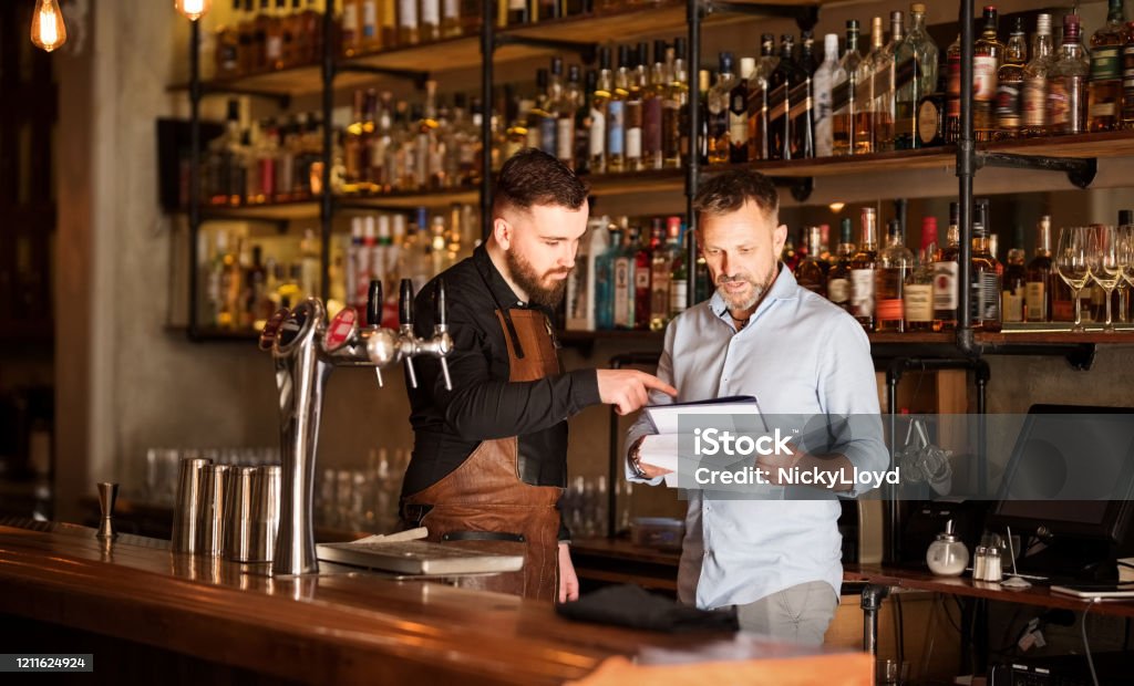 Keeping track of the stock Shot of a bar manager and bartender checking the stock in the pub Restaurant Stock Photo
