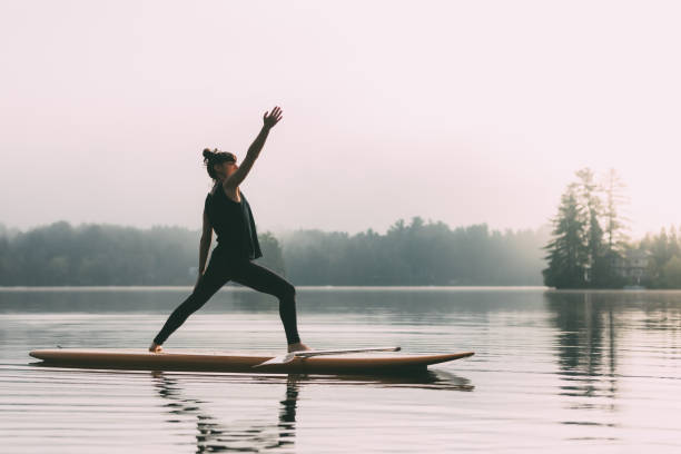 Young Woman Practicing Yoga On A Paddleboard Young Woman practicing SUP yoga on a quiet Lake. paddleboard photos stock pictures, royalty-free photos & images