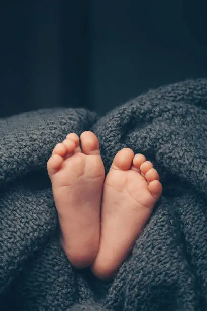 Photo of Soft newborn baby feet against a dark grey blanket, closeup