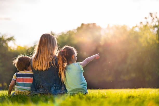 istock Rear view women and two kids sitting on grass 1211632533