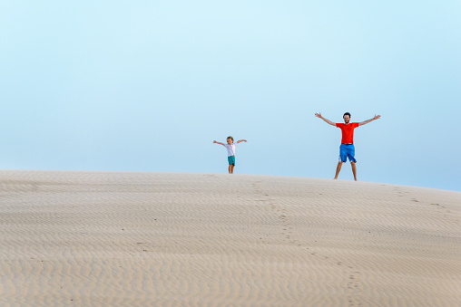 Travelling family, father and son with open arms on a sand dune, enjoying the warm wind in Piauí.