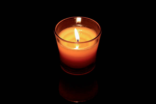 horizontal  image of a small jar with a scented candle burning surrounded by a black background with lots of copy space.