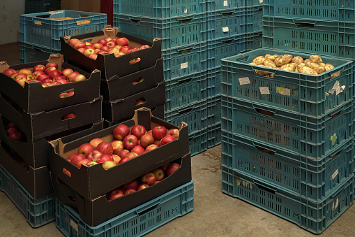 Stacks of plastic box containers with apples, potatoes and other crops in fruit and vegetables warehouse.