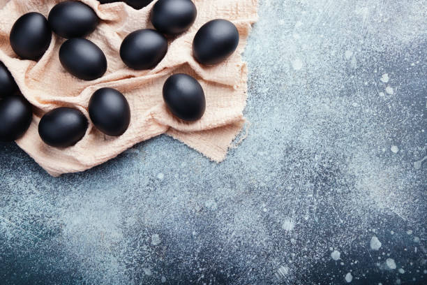 Black Easter eggs on a linen napkin on a blue texture table. Easter celebration concept. Copy space