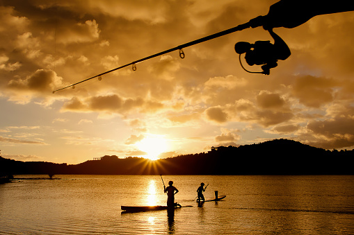 Silhouette of fishermen and fishing rods, with the sunset and the sun sphere in the background