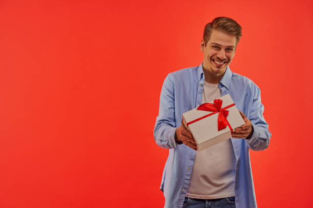 istock Happy guy with a beard in a blue shirt gives a present in a white box. 1211640199