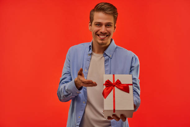 istock Happy guy with a beard in a blue shirt gives a present in a white box. 1211640350