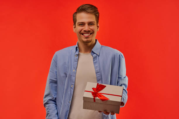 istock A smiling guy with a beard in a blue shirt holds a present in a white box in his left hand. 1211640361