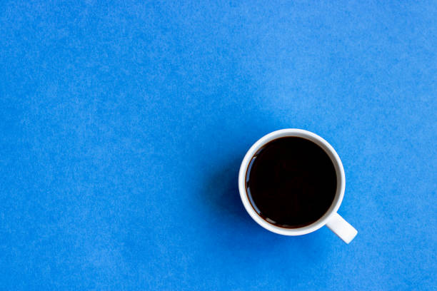Black coffee in white cup on the blue background. Copy space. Top view.