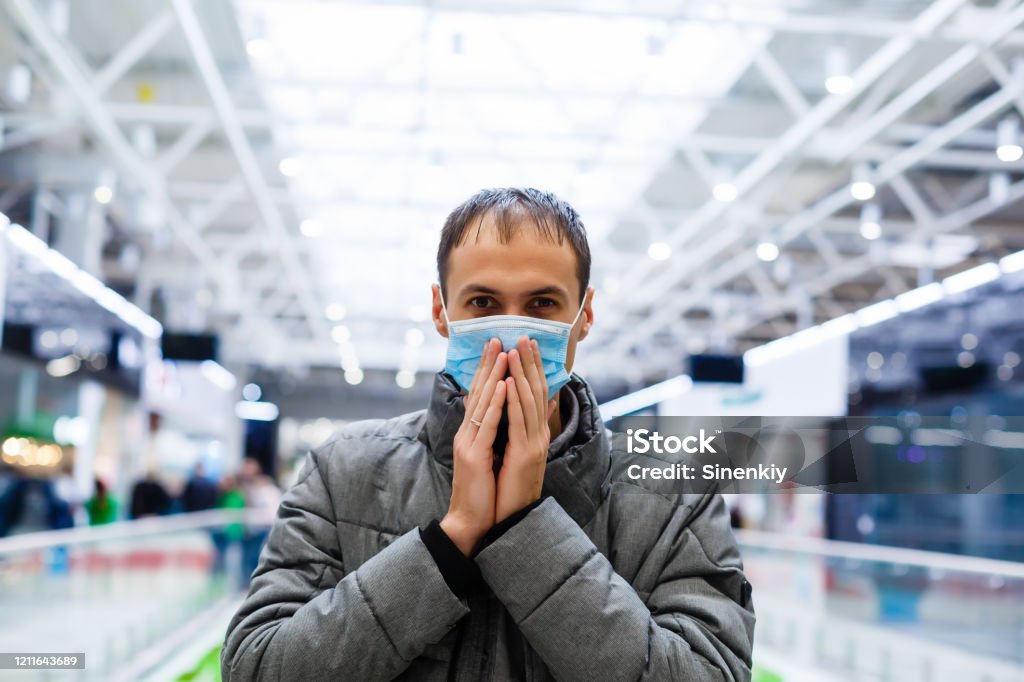 A young man in a medical mask in a shopping center. The masked man protects himself from the epidemic of the Chinese virus "2019-nKoV" Adult Stock Photo