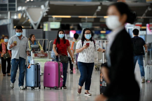 Air Travelers Wear Masks as a Precaution against Covid-19 Bangkok, Thailand - February 18, 2020: Air travelers wearing masks walk through departures hall of Suvarnabhumi Airport. Thailand has been assessed as a country at risk of Covid-19 outside of China. asian tourist stock pictures, royalty-free photos & images